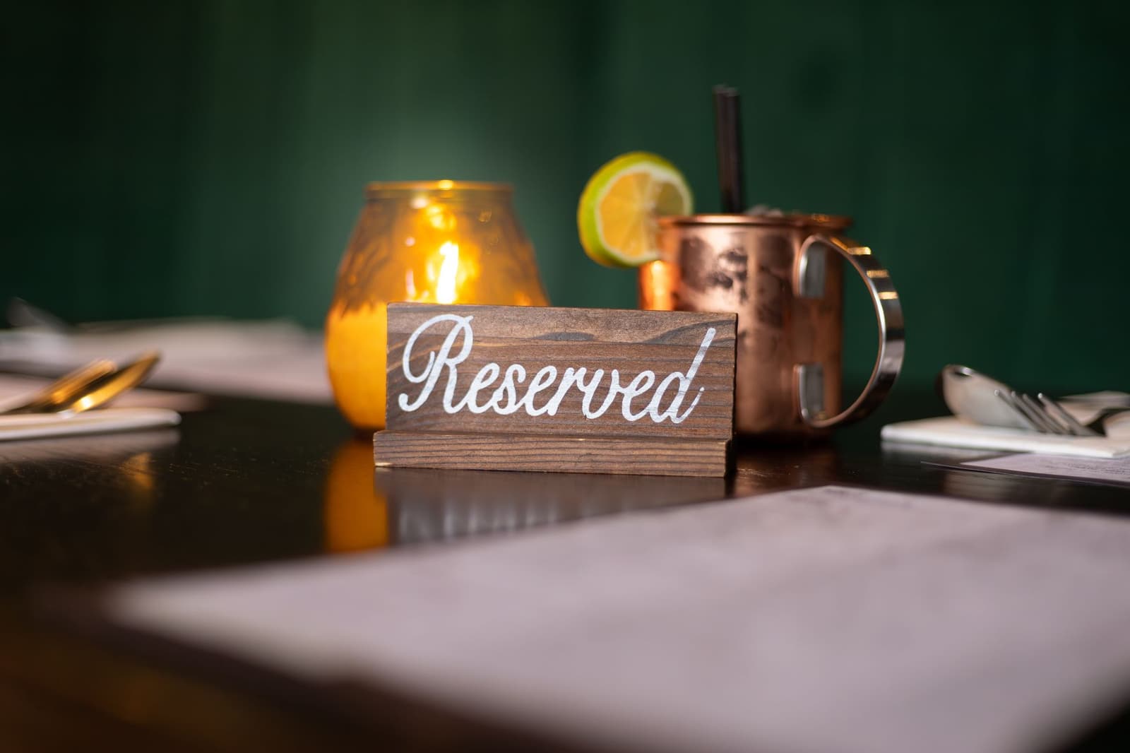 Een houten gereserveerd-bordje op een restauranttafel naast kaars en cocktail