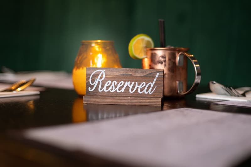 Een houten gereserveerd-bordje op een restauranttafel naast kaars en cocktail