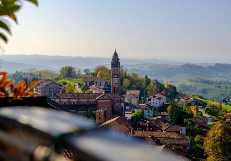 Pueblo en un alto del Piamonte con campanario y viñedos otoñales al fondo