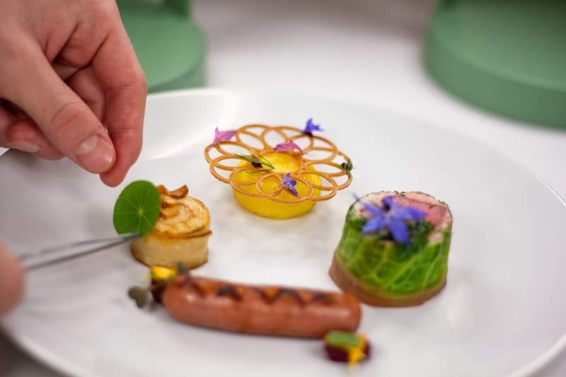 Main d'un chef dressant un plat de menu dégustation avec des fleurs comestibles sur une assiette blanche