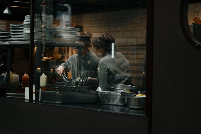 Deux chefs dressant des assiettes ensemble, vus à travers la fenêtre du pass d'une cuisine de restaurant