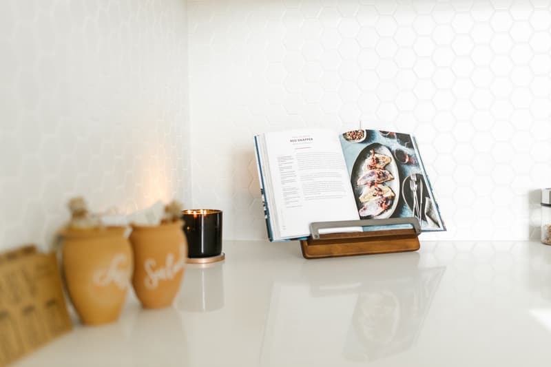 An open cookbook on a wooden stand on a kitchen counter