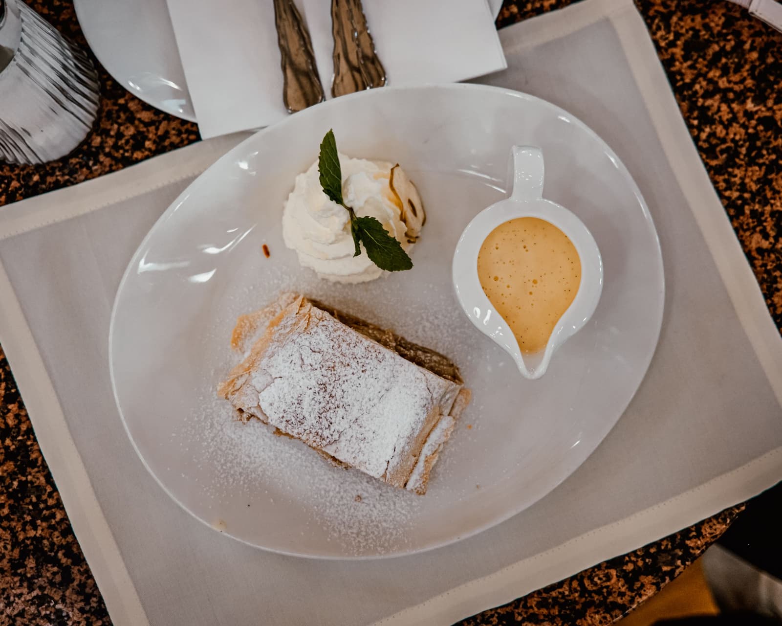 Stuk appelstrudel met poedersuiker, slagroom en een kannetje vanillesaus