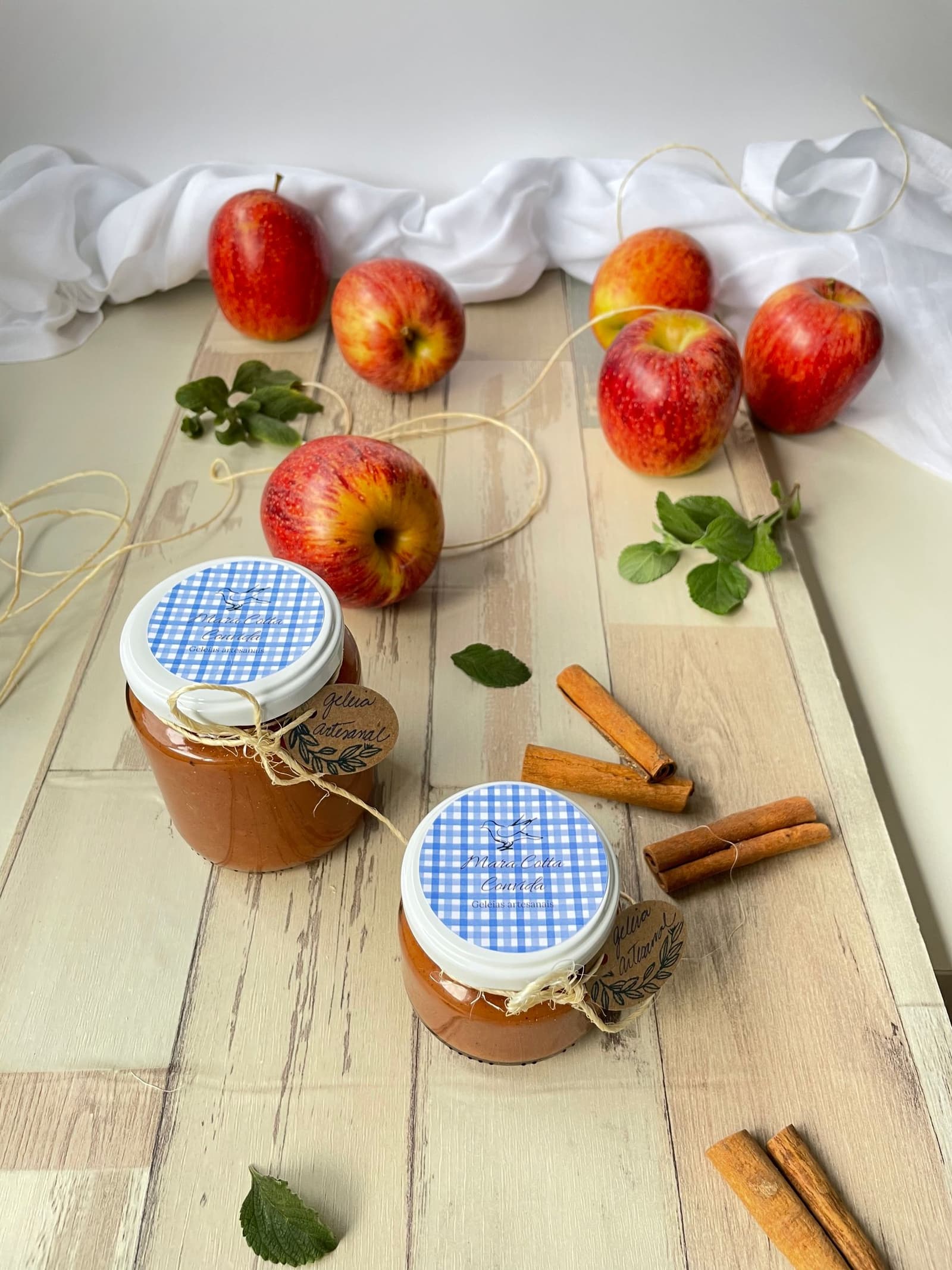 Tarros de cristal con compota de manzana junto a manzanas frescas y ramas de canela