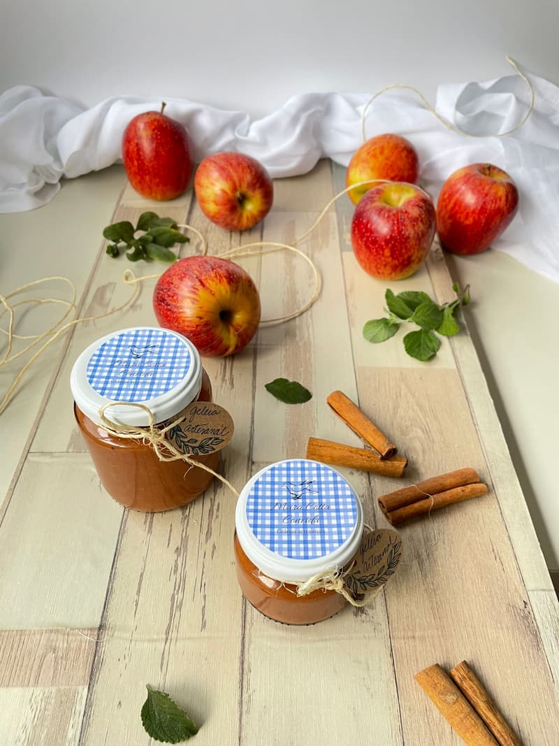 Glazen potten appelmoes naast verse appels en kaneelstokjes op een houten tafel