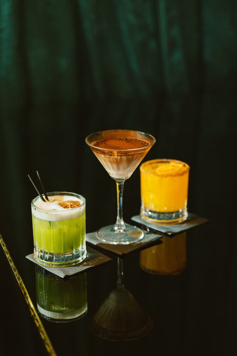 Tre cocktail colorati in bicchieri diversi su un bancone scuro e riflettente