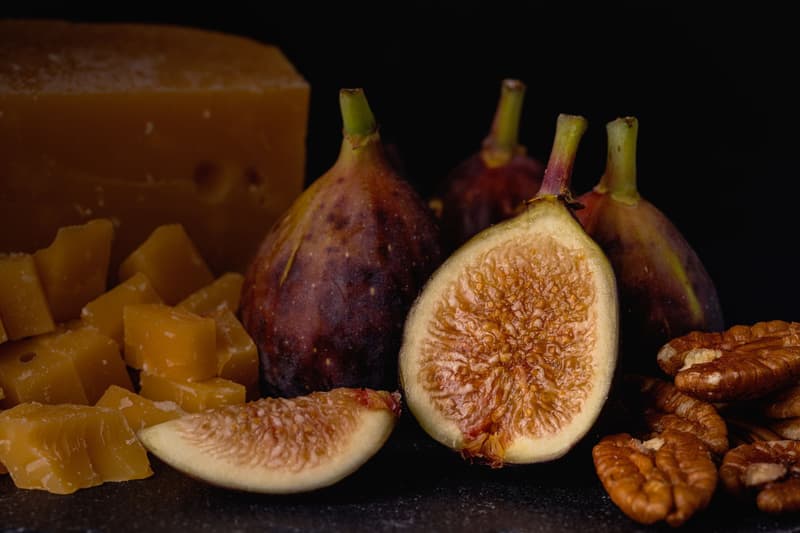 Higos enteros y partidos junto a un bloque de queso y pistachos pelados