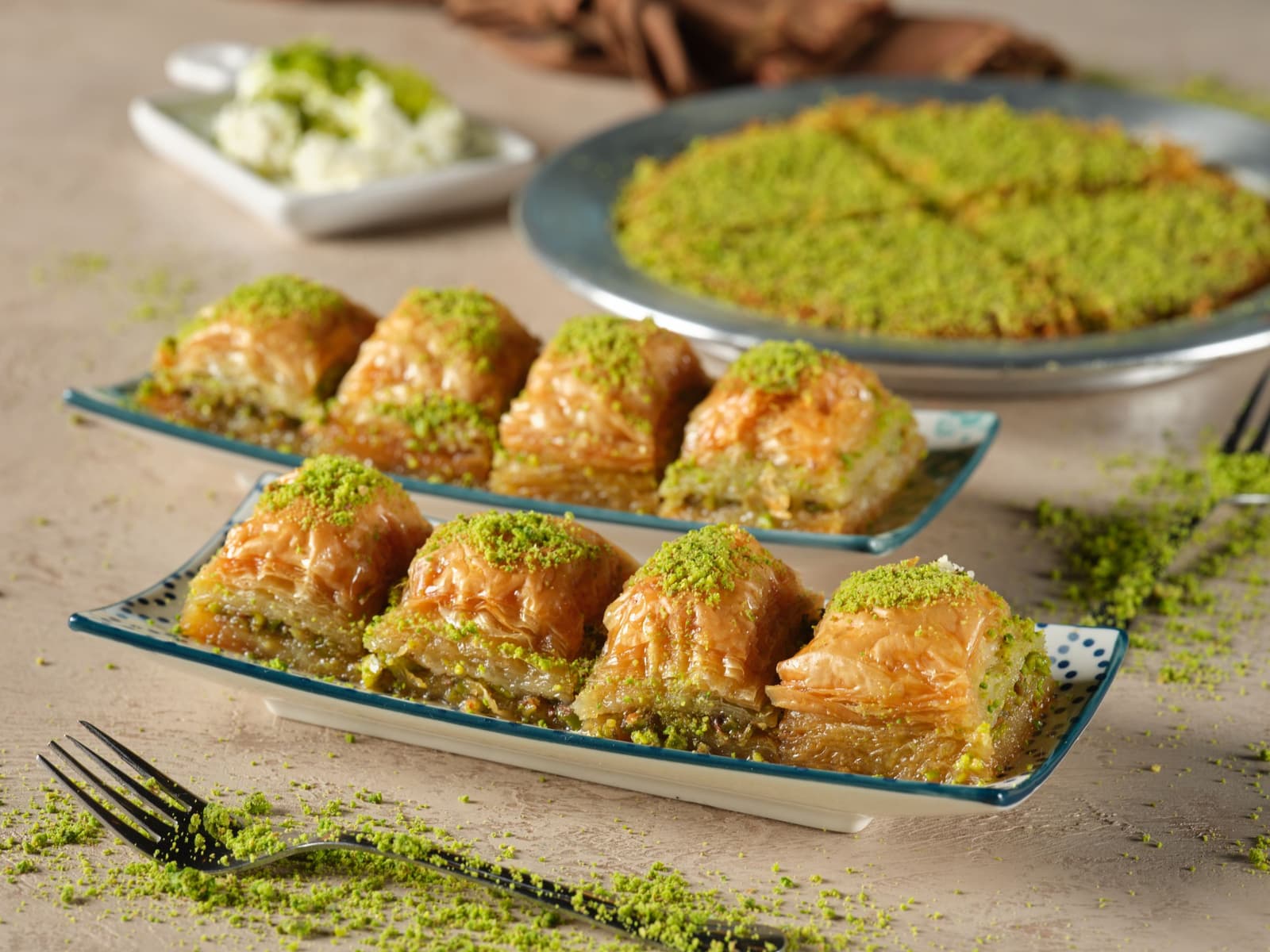Porciones cuadradas de baklava de pistacho en dos platos de borde azul, cubiertas de pistacho molido