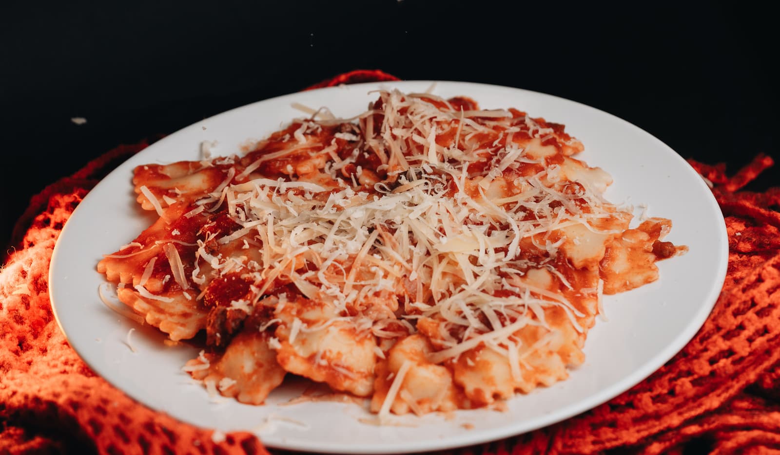 Primer plano de ravioli de ricotta en salsa de tomate con queso rallado sobre un plato blanco