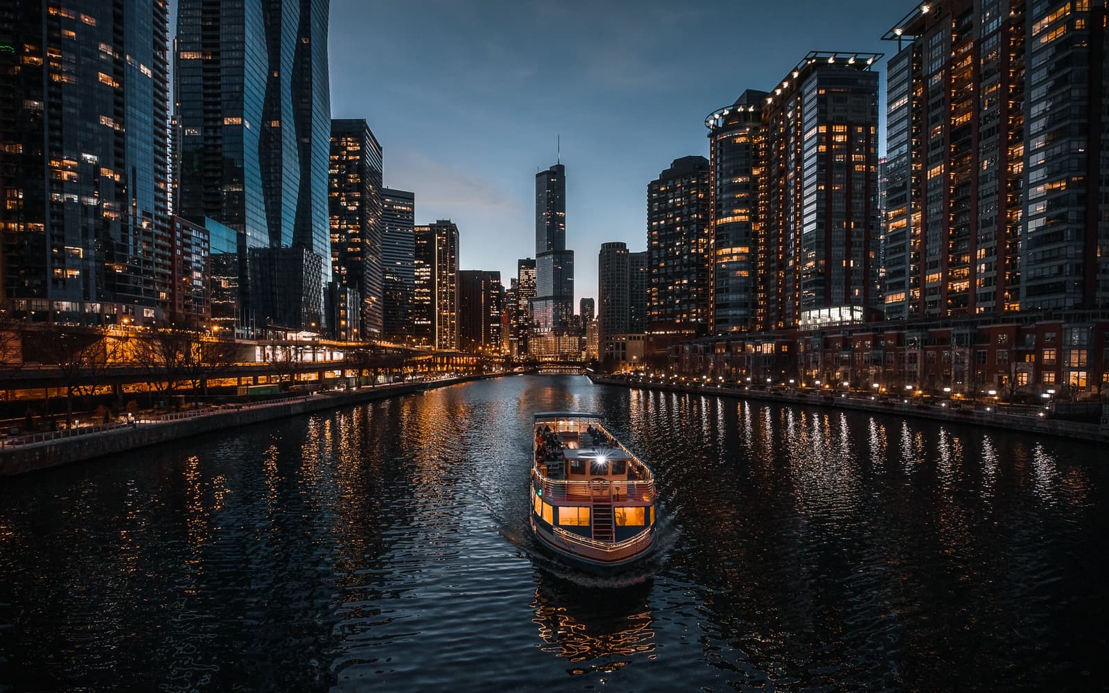 Il fiume Chicago al tramonto con un battello turistico illuminato tra grattacieli accesi