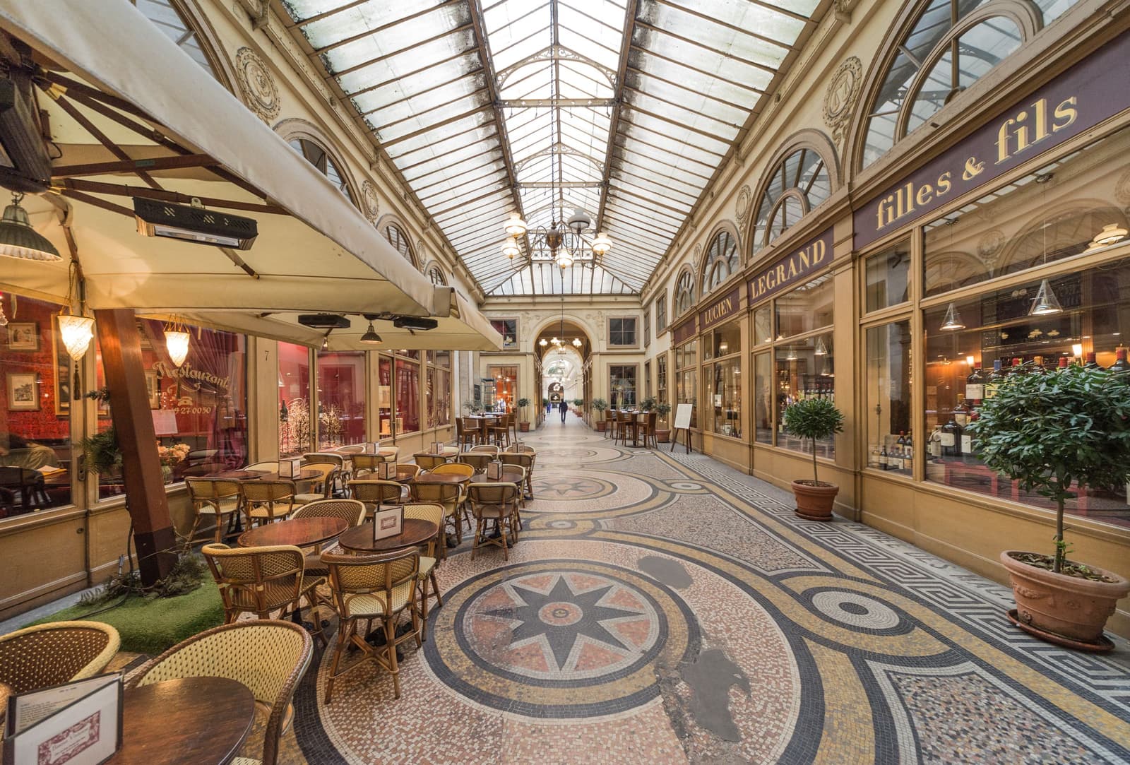 Empty café tables under the glass roof and mosaic floor of a covered passage in Paris