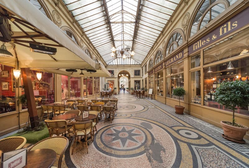 Lege caféterrastafels onder het glazen dak en op de mozaïekvloer van een overdekte passage in Parijs
