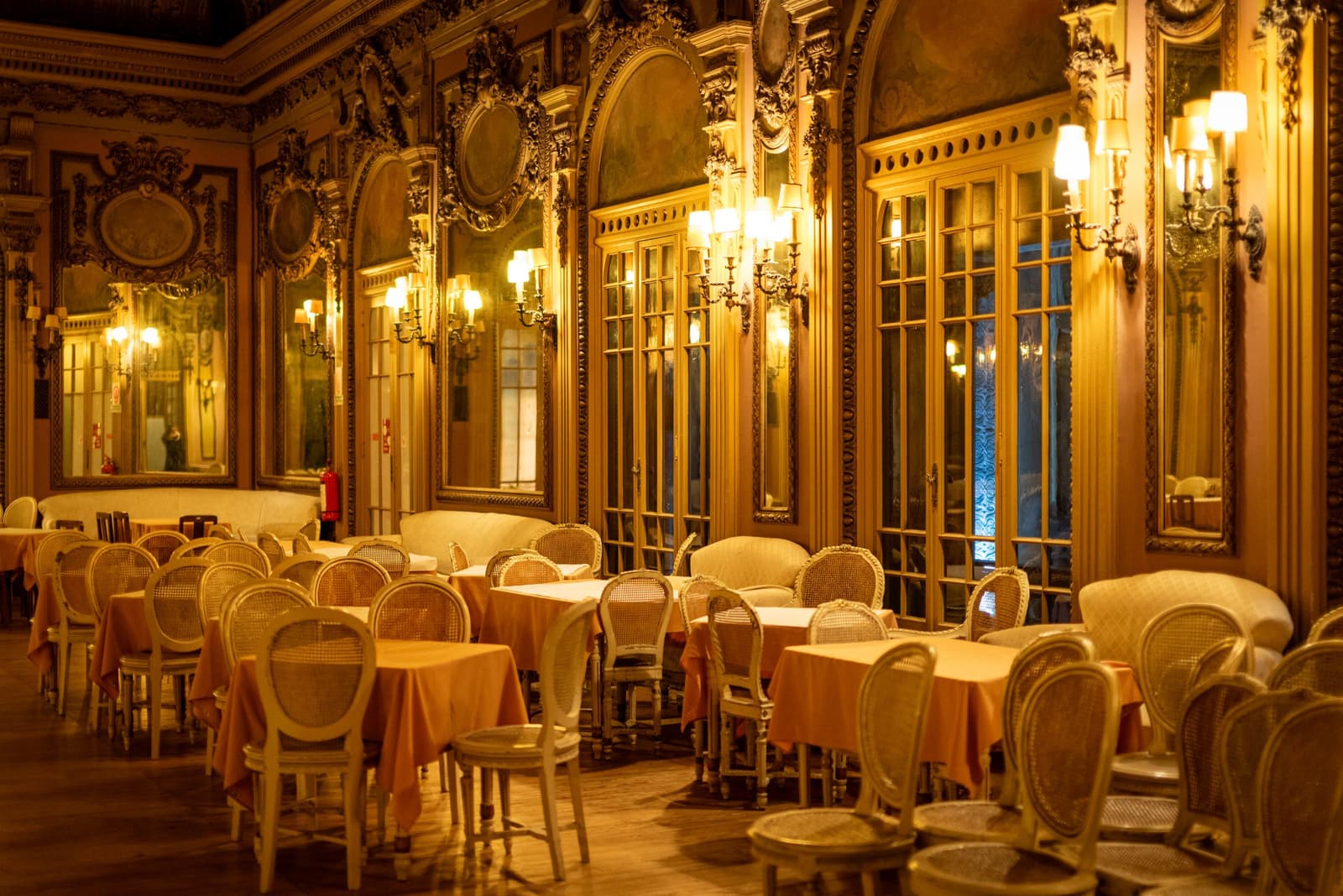 Empty gilded dining room with mirrors, wall lamps and cane chairs in a historic Lisbon restaurant