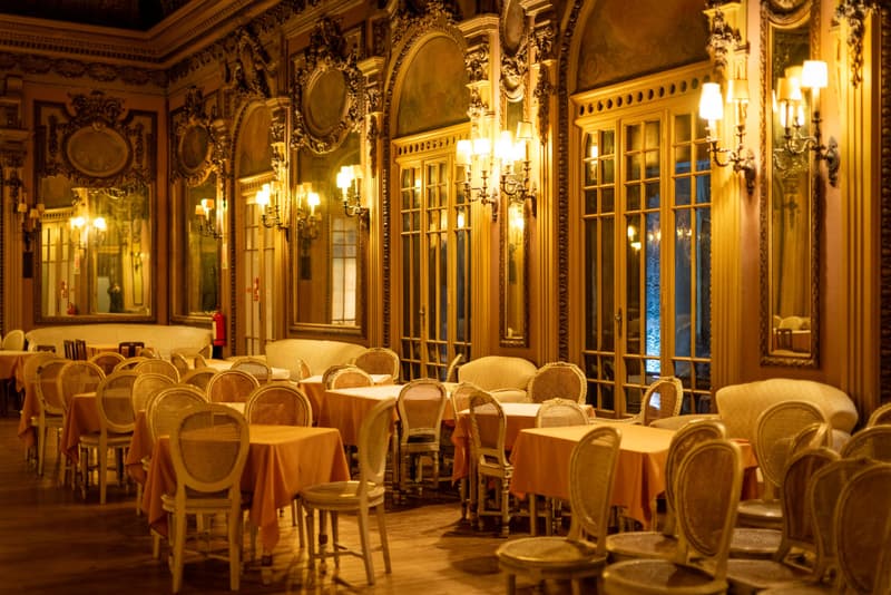 Comedor dorado y vacío con espejos, apliques y sillas de rejilla en un restaurante histórico de Lisboa
