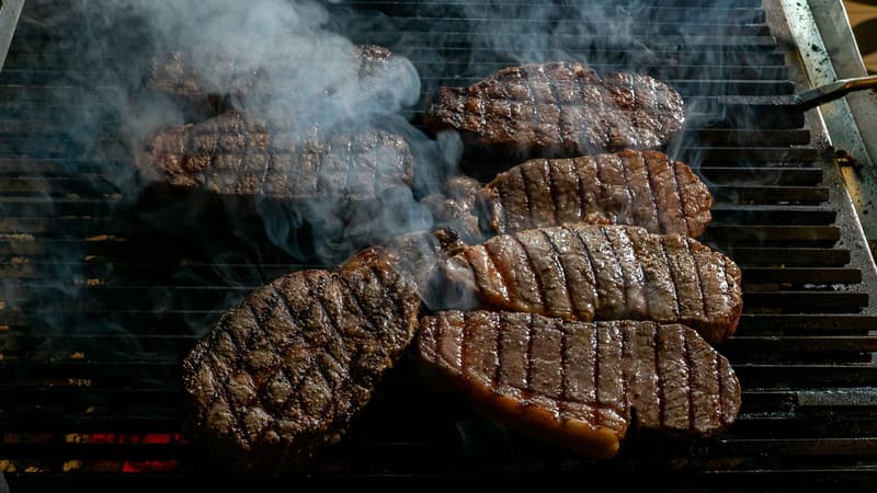 Varios filetes de ternera dorándose en una parrilla de carbón con humo