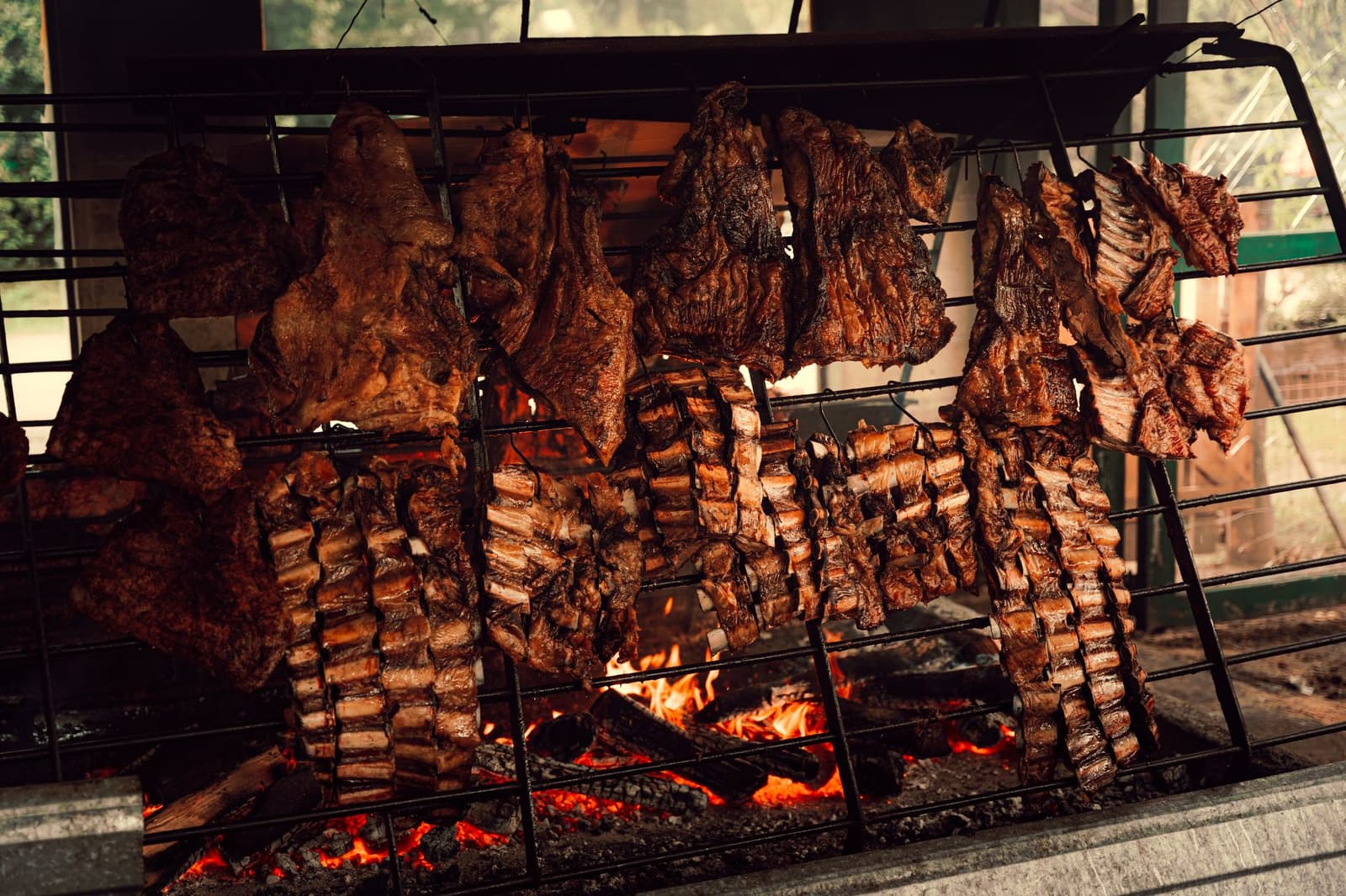 Costillas y cortes de asado argentino colgados sobre un fuego de leña