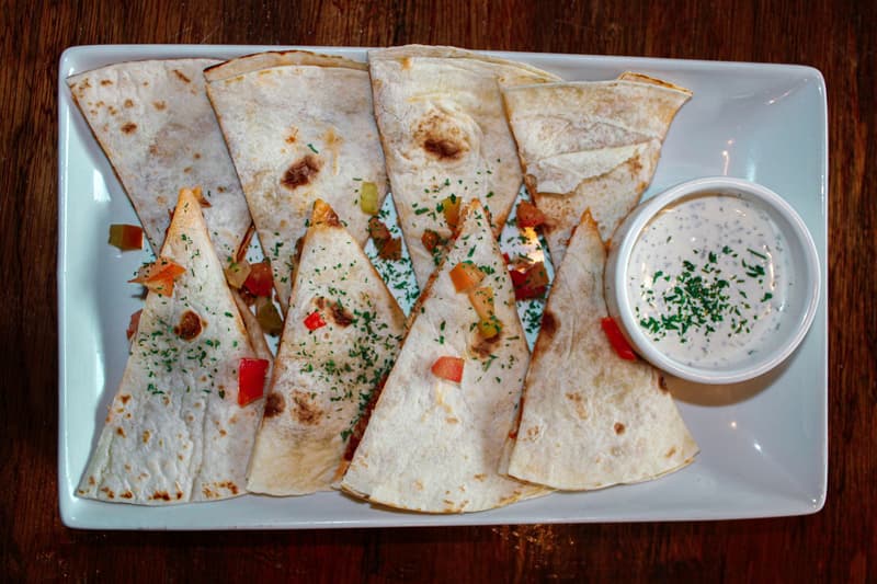 Käse-Quesadilla-Ecken auf einem Teller mit einer Schale cremigem Dip