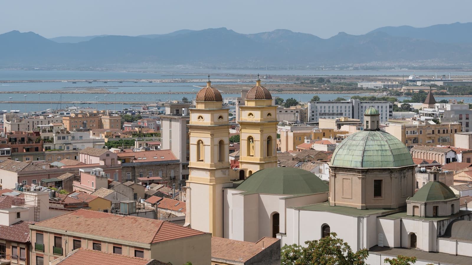 Rooftops and church domes of Cagliari with the harbour and mountains behind