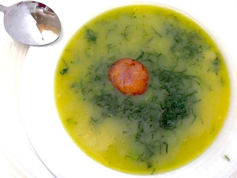 Cuenco de caldo verde con hojas en tiras finas, aceite de oliva y una rodaja de chouriço