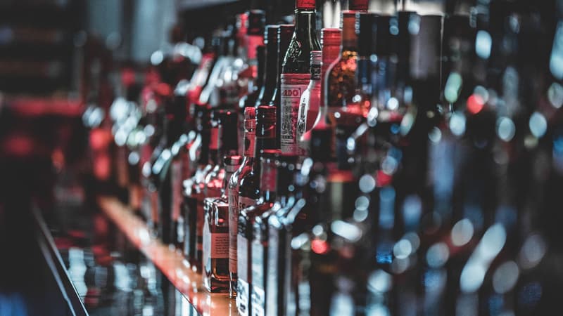 Rangée de bouteilles de spiritueux sur une étagère de bar éclairée, la plupart floues