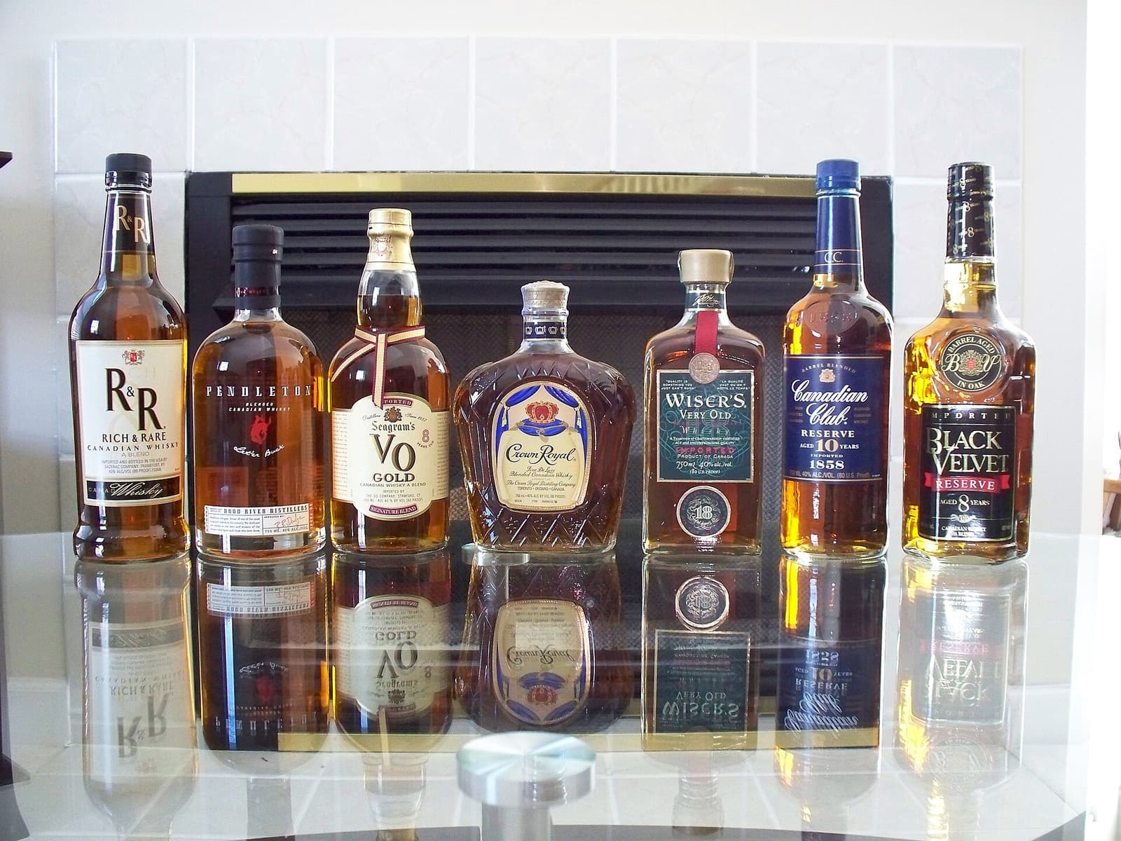 Zeven flessen Canadese whisky, waaronder Crown Royal, op een rij op een glazen tafel