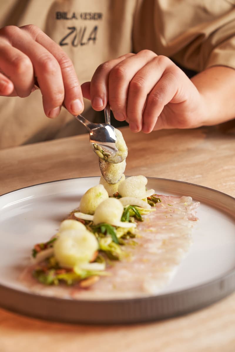 Le mani di uno chef impiattano una delicata portata di un menu degustazione con un cucchiaio