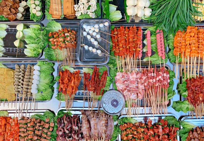 File di spiedini crudi di carne, tofu e verdure esposti in una bancarella di street food a Chengdu