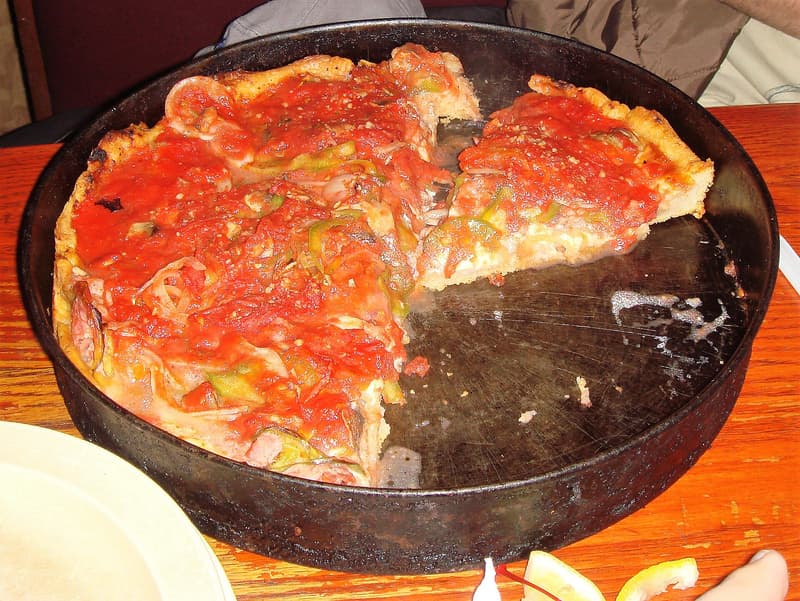 Chicagoer Deep-Dish-Pizza mit Tomatensoße in der Stahlform, ein Stück herausgehoben