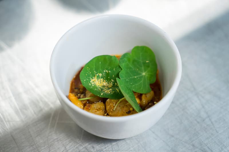A single fine-dining course in a white bowl on a steel counter