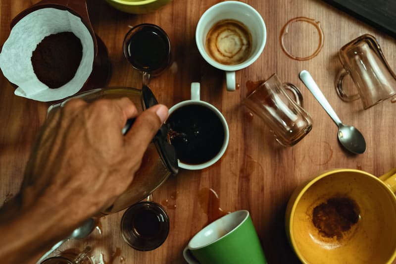 A hand pours filter coffee into a cup among several tasting cups on a wooden table