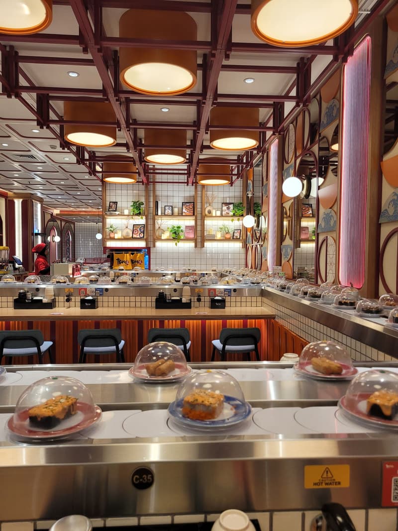 Interno di un ristorante di sushi con nastro trasportatore, piatti coperti e sgabelli al bancone