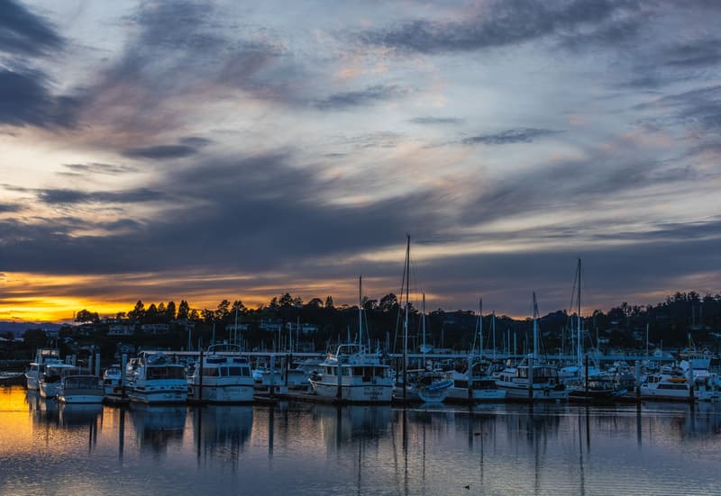Bateaux amarrés dans un port de plaisance au crépuscule avec un coucher de soleil orange à l'horizon