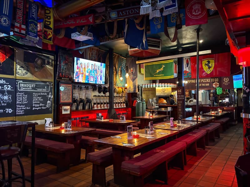 Une salle de sports bar avec tables en box, écrans et étagères de tireuses à bière