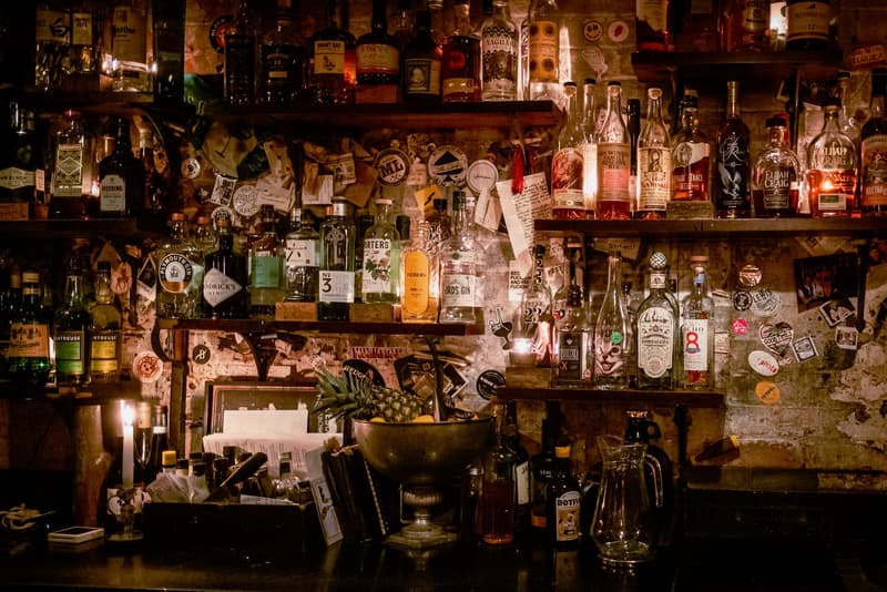 Scaffale del bancone affollato di bottiglie di liquore e adesivi in un bar in stile speakeasy poco illuminato