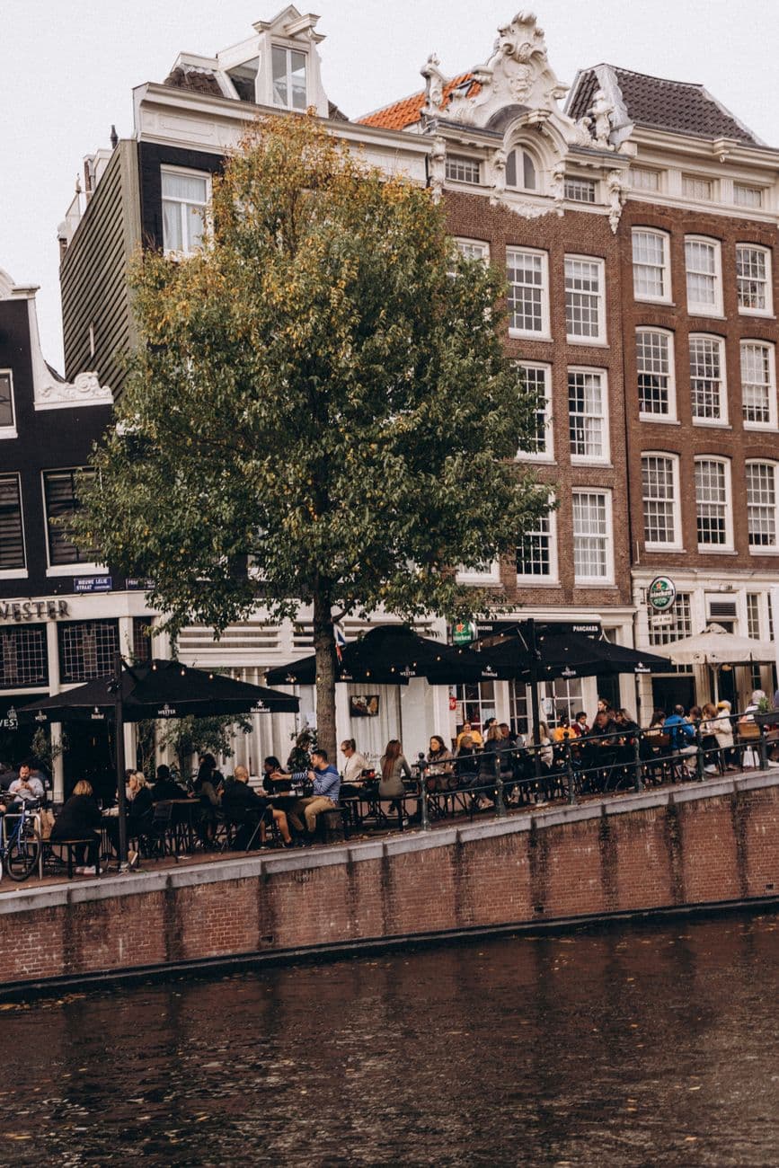 Gasten vullen een terras aan een gracht in het centrum van Amsterdam bij schemer