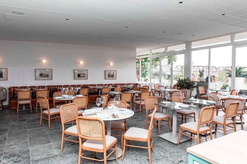 Salle de restaurant vide avec tables dressées, chaises cannées et hautes fenêtres