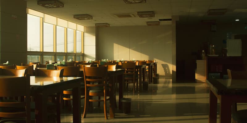Sunlit empty restaurant dining room with wooden tables and chairs