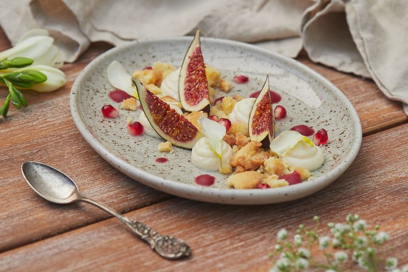 Spicchi di fico con crema, briciole e semi di melograno su un piatto maculato