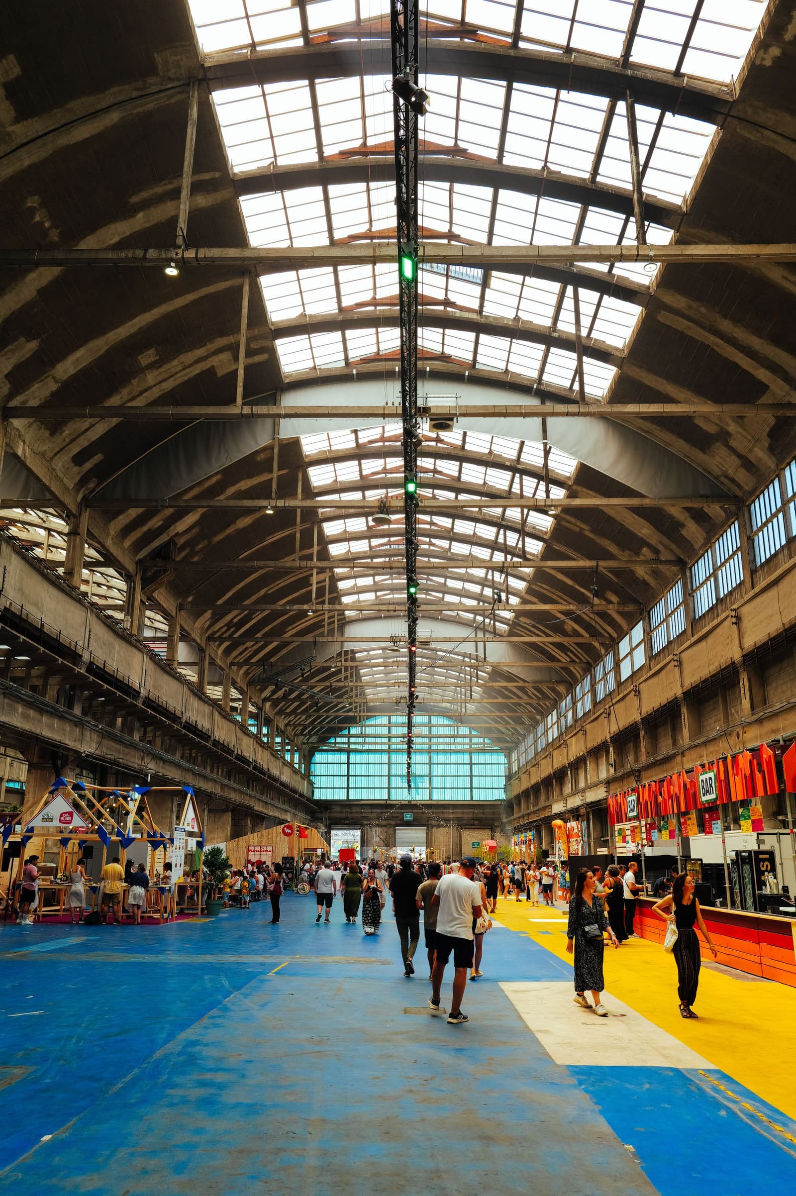 Bezoekers lopen door een grote overdekte beurshal met stands van exposanten