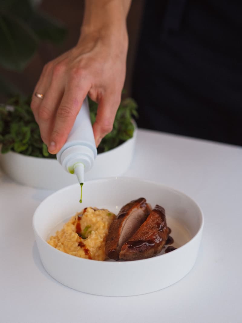 La mano de un chef terminando un plato de alta cocina con un hilo de salsa