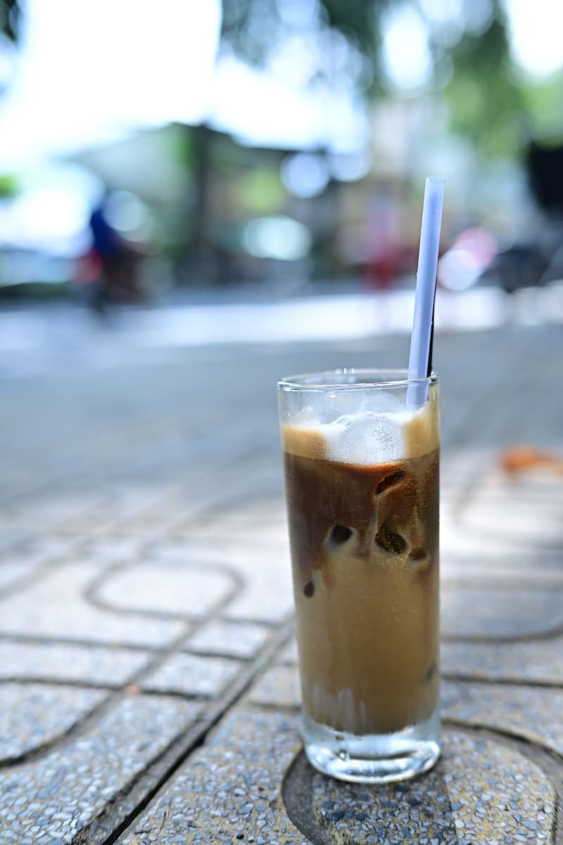 Tall glass of iced coffee with a straw on a street cafe table