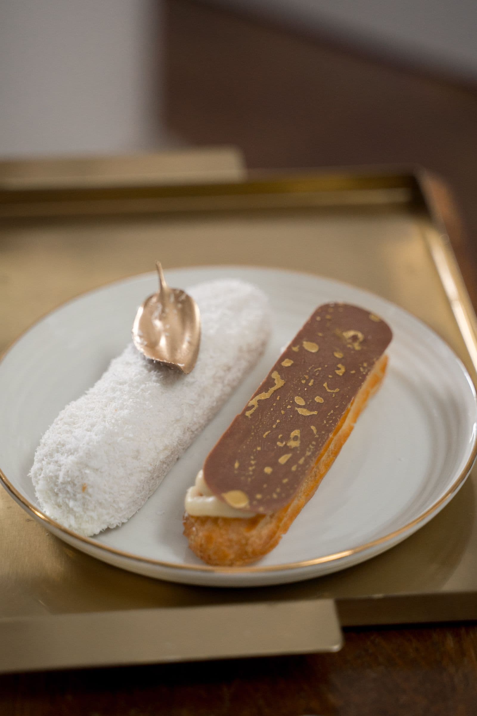 Deux pâtisseries françaises, un éclair et une bûchette à la noix de coco, sur une assiette bordée d'or