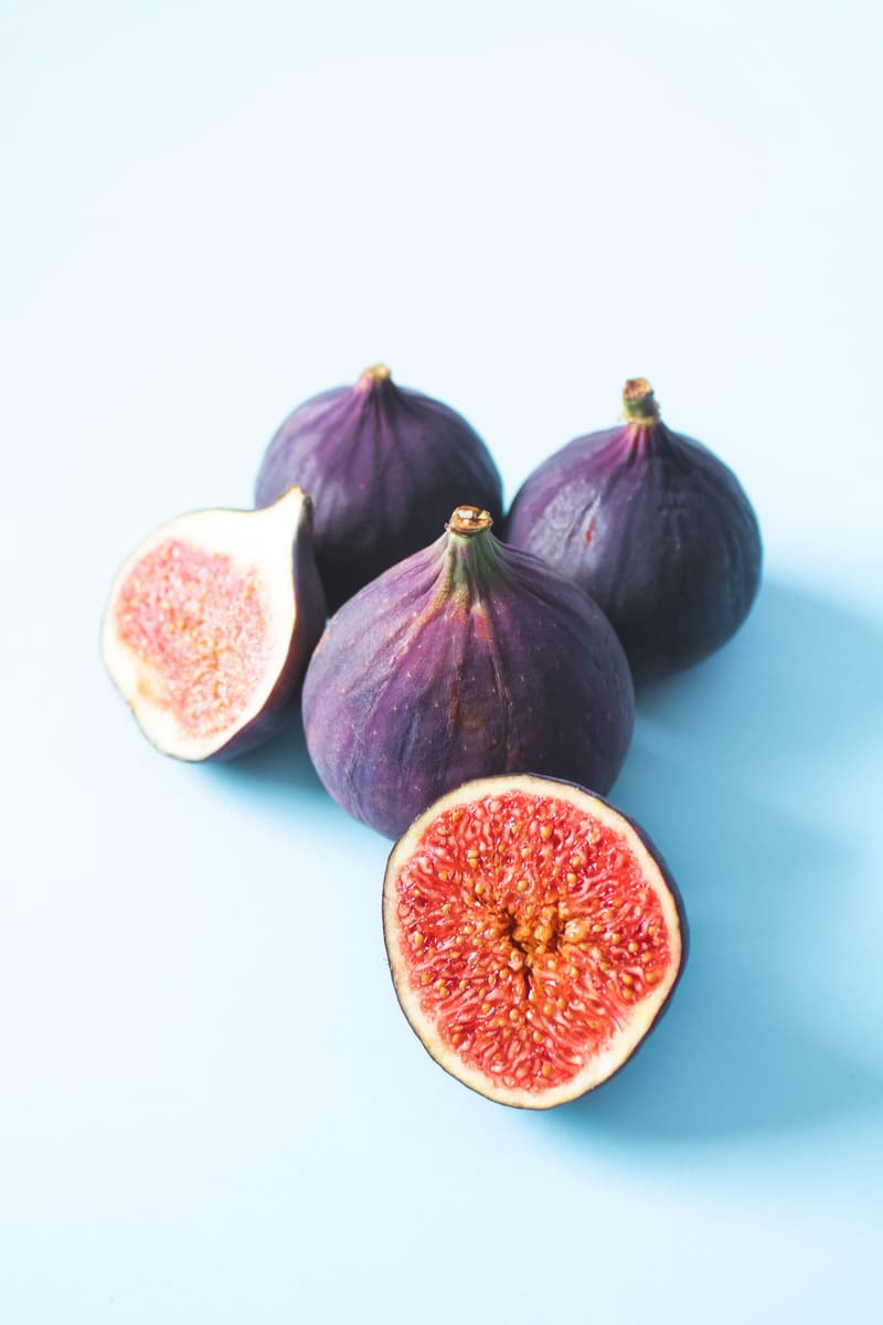 Fichi viola freschi interi e tagliati a metà che mostrano la polpa rossa su uno sfondo azzurro chiaro