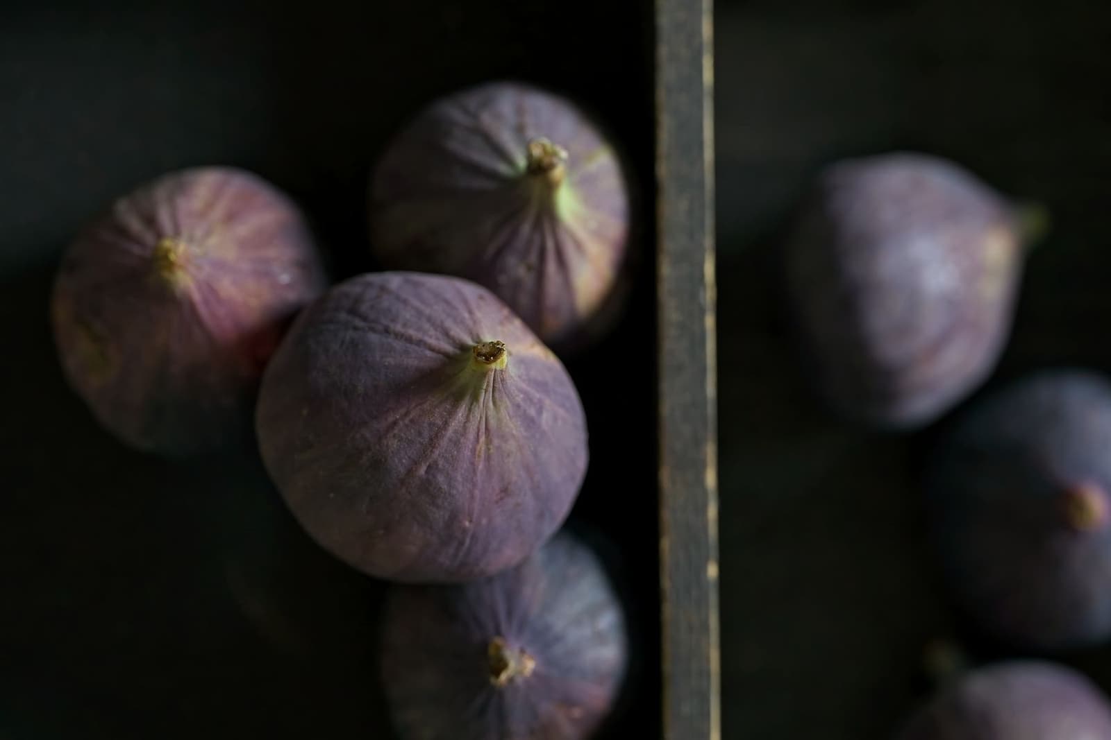 Ripe purple figs stacked together in a dark wooden crate