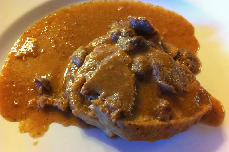 Fricandó di vitello con piccoli funghi in una salsa bruna e densa su un piatto bianco