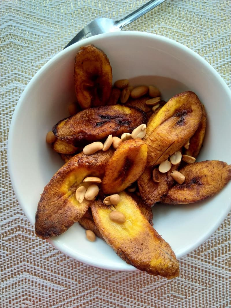 Una ciotola di fette di platano fritto dorato guarnite con arachidi tostate
