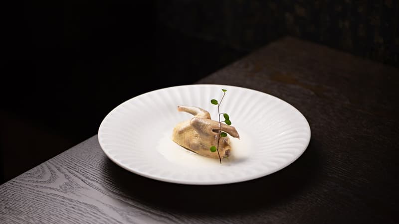 Codorniz asada entera en un plato blanco estriado en un comedor oscuro