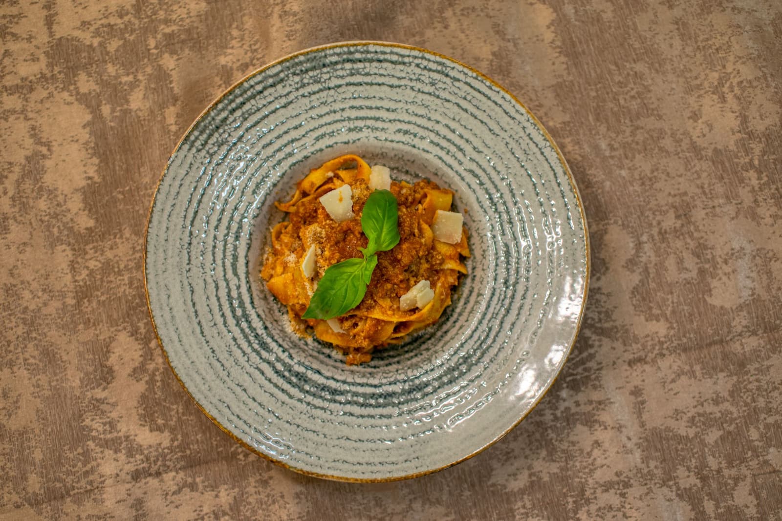 Tagliatelle al ragù di carne con basilico e scaglie di parmigiano su un piatto grigio
