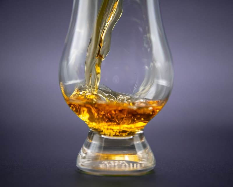 Whisky ambrato versato in un bicchiere da degustazione Glencairn su sfondo scuro