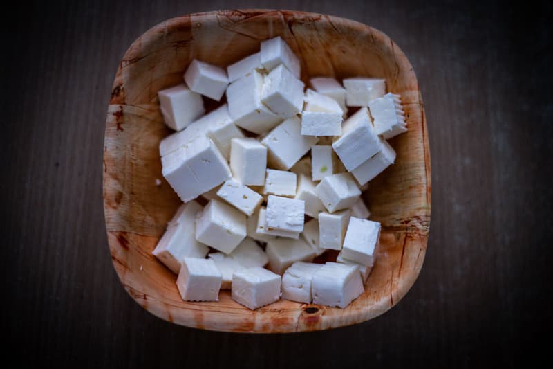 Cubetti di feta bianca ammucchiati in una ciotola quadrata di legno su un tavolo scuro